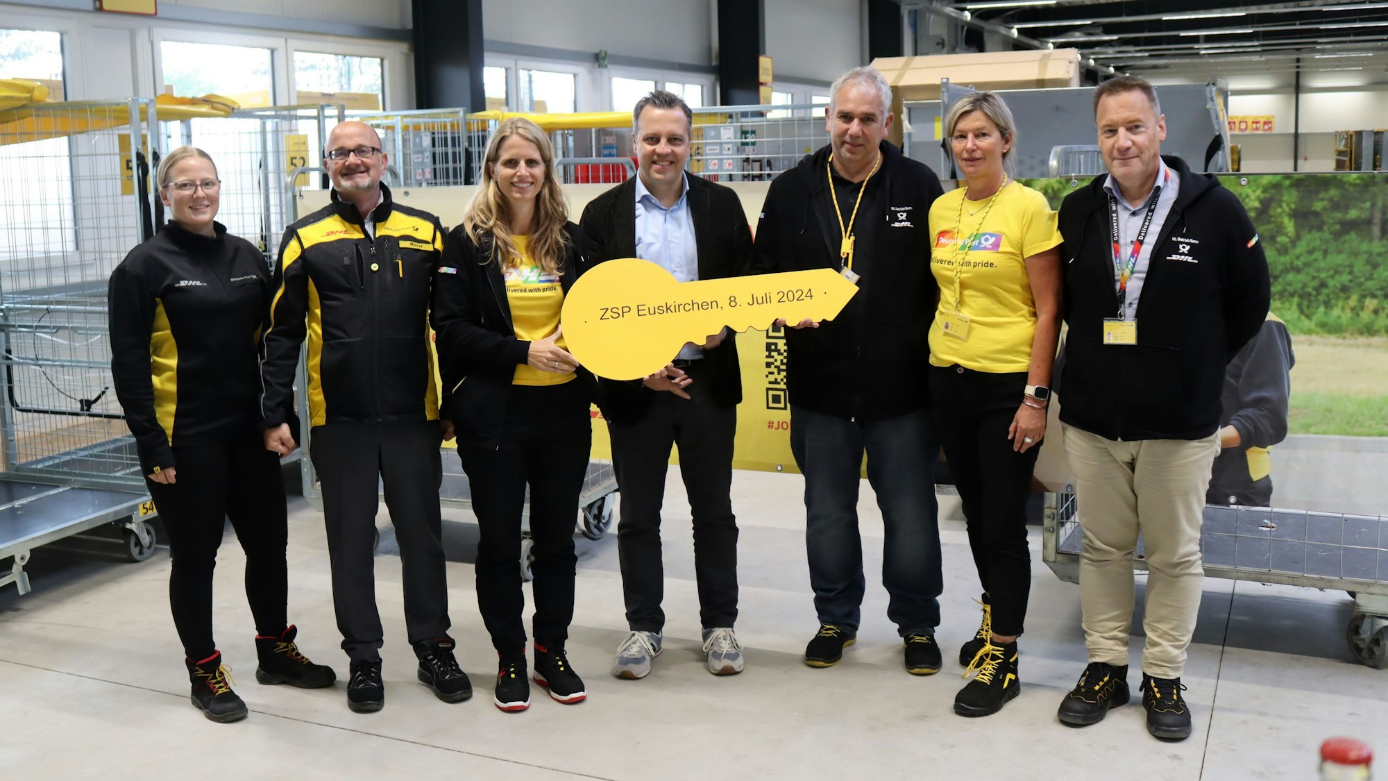 Sechs Mitarbeiter der Post und Euskirchens Bürgermeister posieren für ein Gruppenfoto. Der Bürgermeister hält einen riesigen gelben Schlüssel in den Händen.
