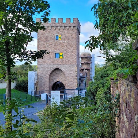 Hinter Büschen und Bäumen sieht man das neue Weiertor mit zwei Fenstern und grün-gelben Fensterläden.