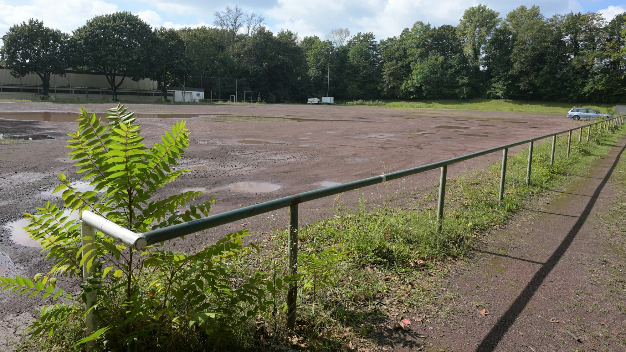 Im Vordergrund ist das Geländer des Aschenplatzes zu sehen. Auf dem Platz parkt ein Auto.