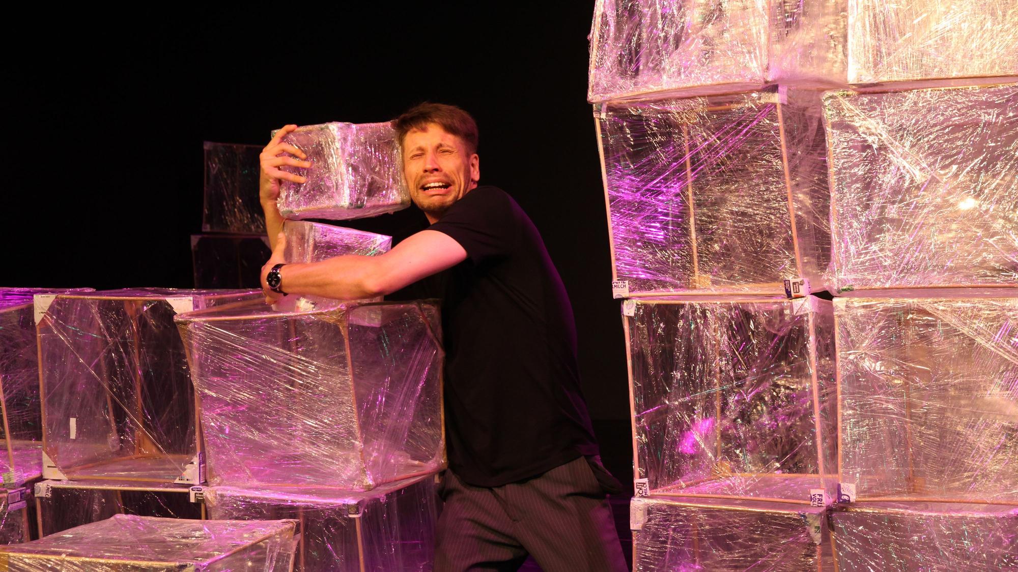Ein Schauspieler umarmt einen Würfel aus Kunststofffolie.
