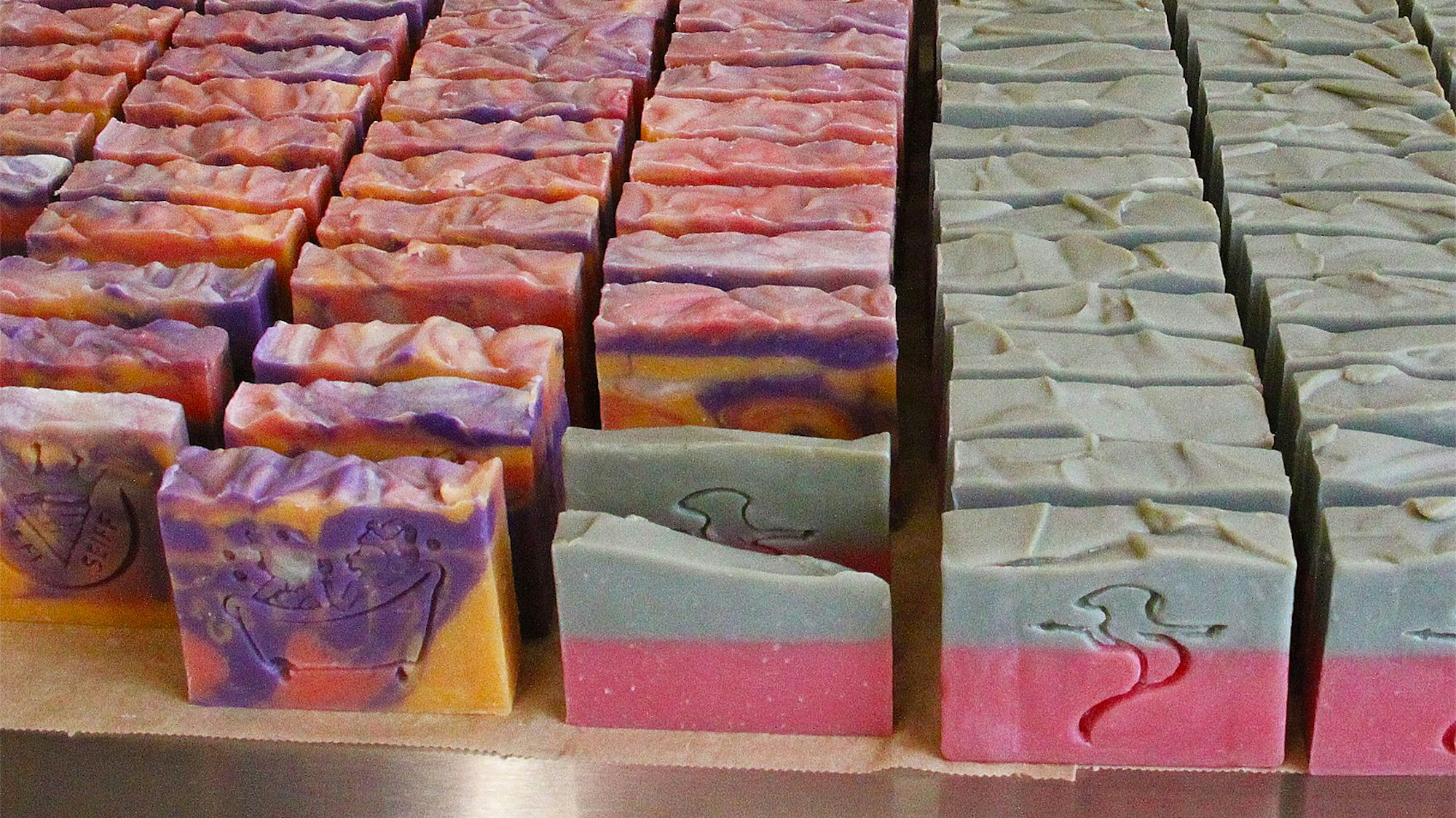 Zahlreiche verschiedenfarbige Seifenblöcke mit unterschiedlichen Prägungen stehen hintereinander.