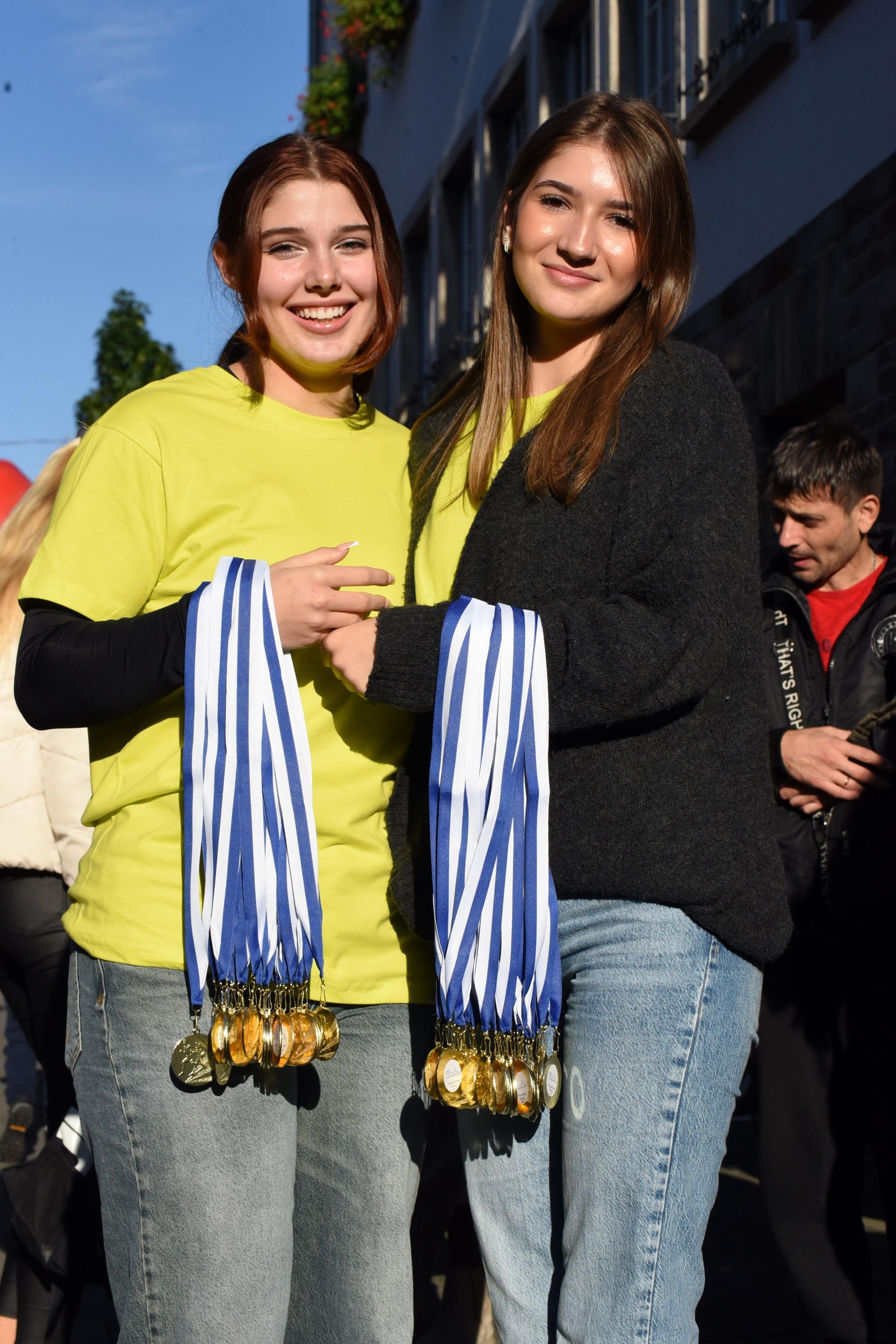Zu sehen sind zwei junge Frauen, die jeweils viele Medaillen an ihrem Arm tragen.
