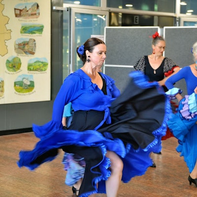 Drei Frauen mit Flamenco-Kleidern und ernstem Gesichtsausdruck zeigen einen Tanz.