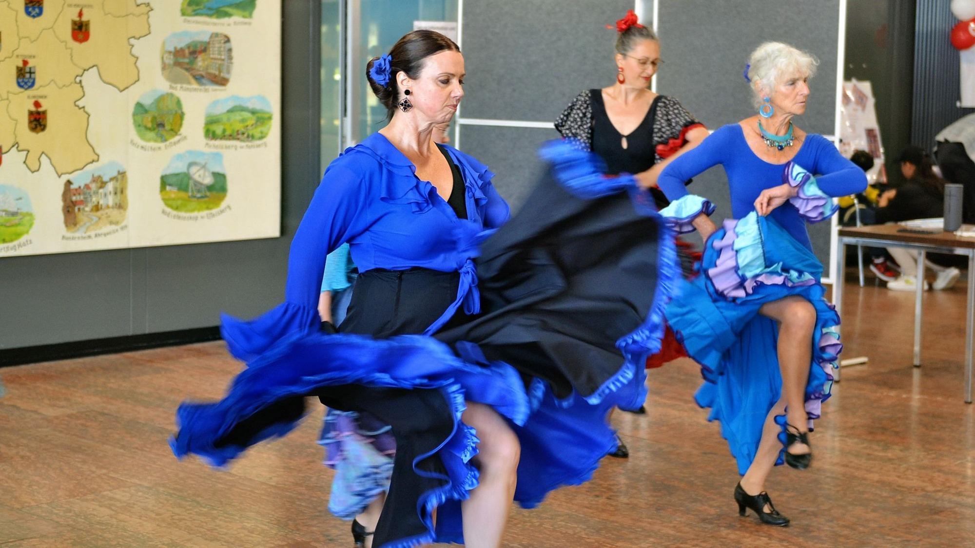 Drei Frauen mit Flamenco-Kleidern und ernstem Gesichtsausdruck zeigen einen Tanz.