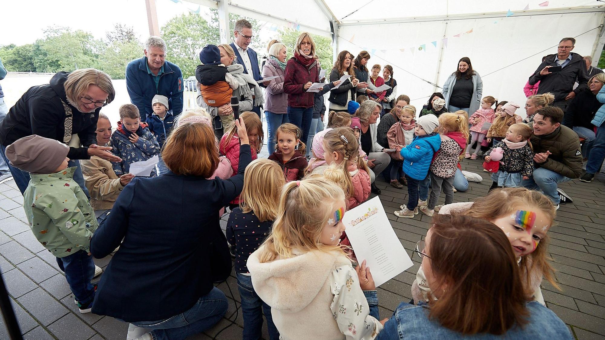 Zahlreiche Kinder stehen in Nettersheim in einem Zelt und singen zur Eröffnung ihrer Kita ein Lied.