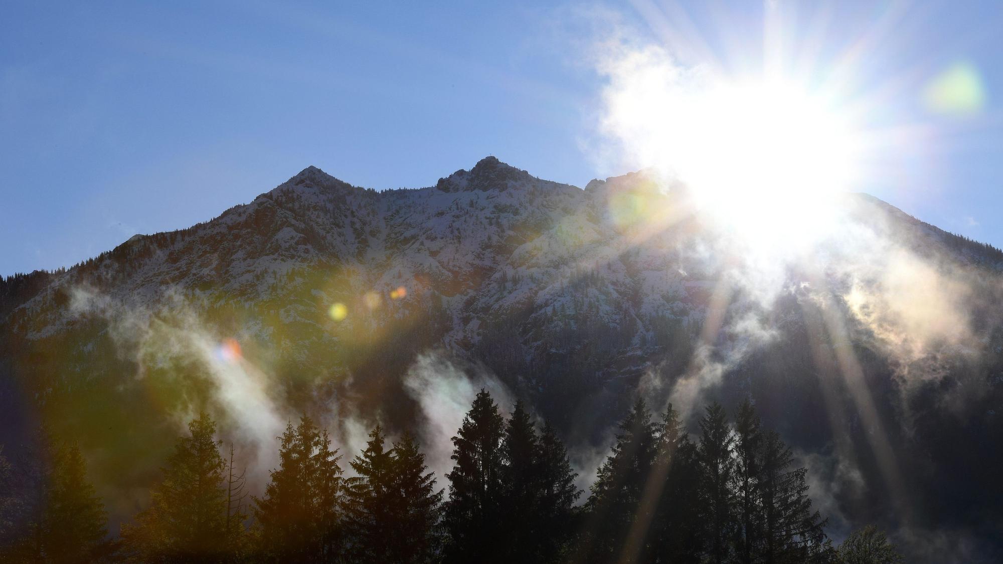 Morgennebel steigt über den Wiesen vor den Gipfeln des schneebedeckten Karwendelgebirges auf.