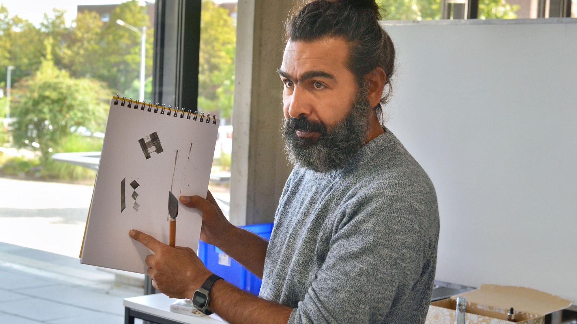 Ibrahim Alsaeid hält einen Block in der Hand und zeigt erste Schritte in arabischer Kalligrafie.