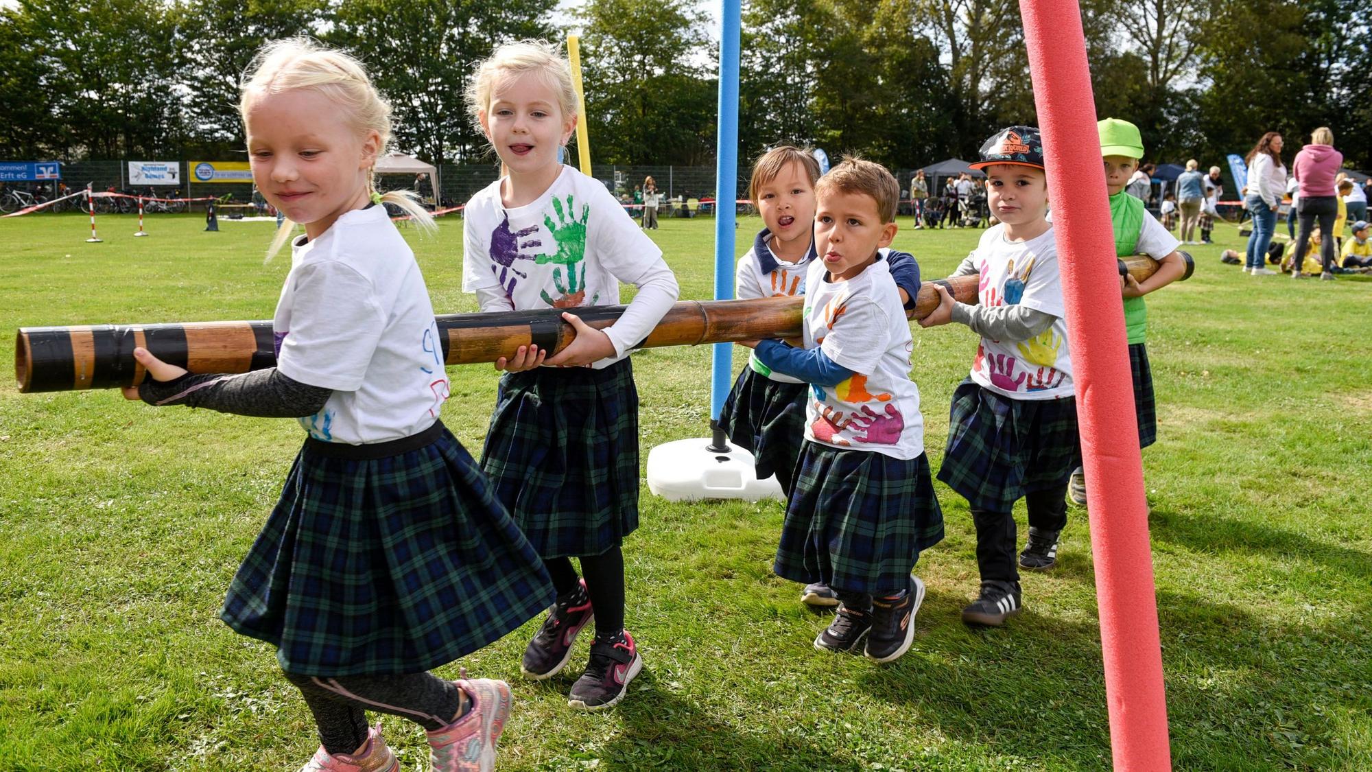 Eine Bambusstange tragen die Kinder durch den Slalomparcours.