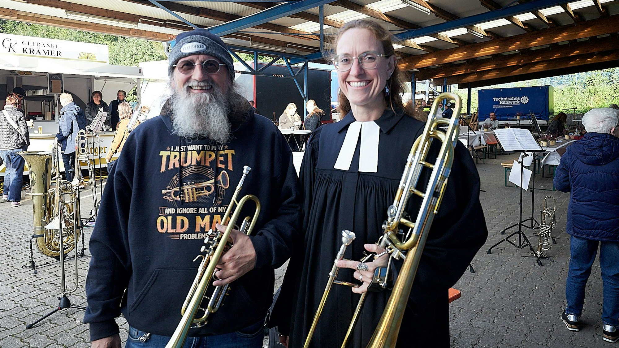 Frank Paqué hat eine Trompete in der Hand, Silja Nagel eine Posaune. Sie stehen vor dem Blaulichtgottesdienst auf dem Gelände des THW in Schleiden.