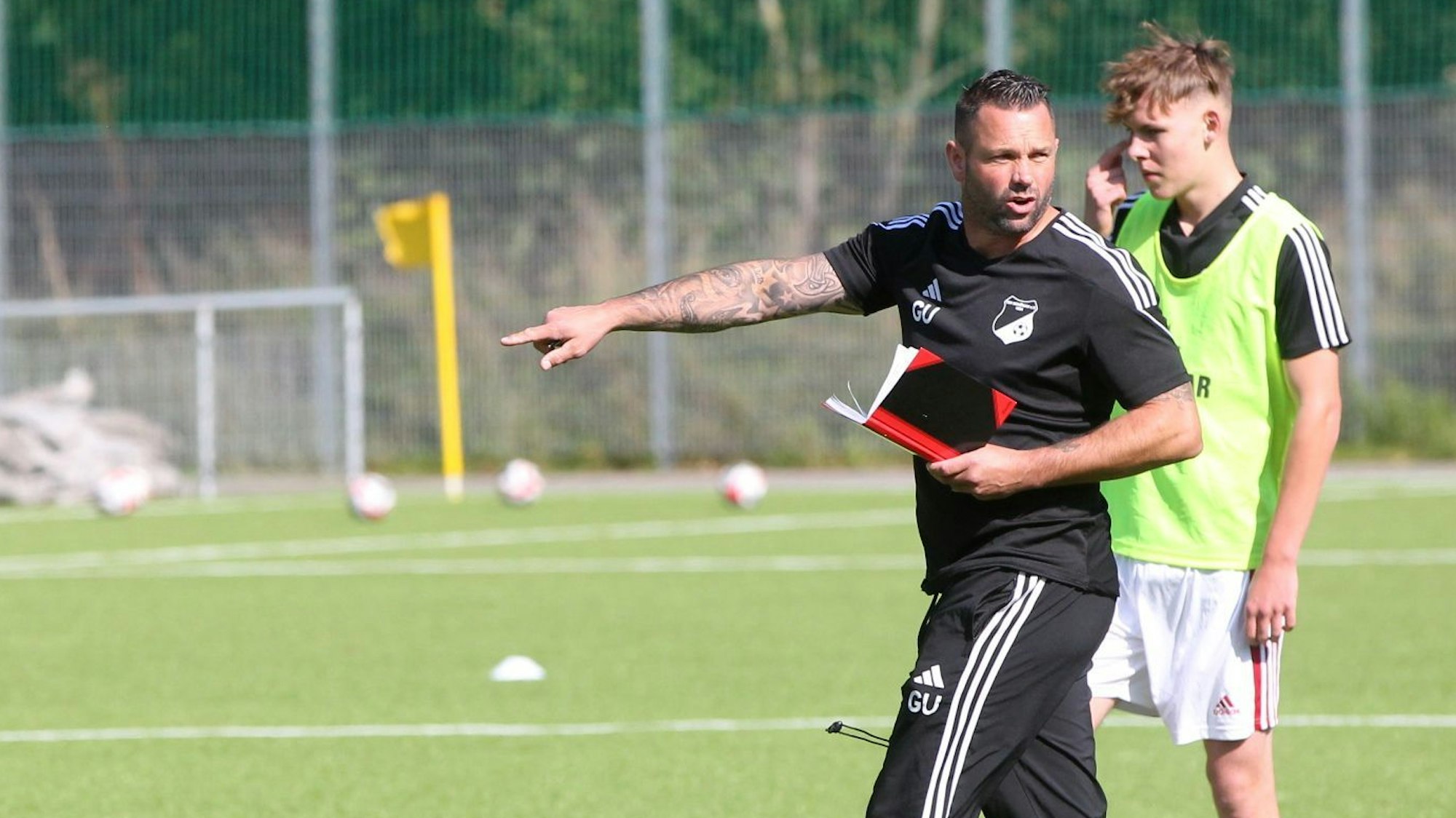 Trainer Gerrit Ueckert hat eine Kladde in der Hand und zeigt mit dem rechten Finger etwas an.