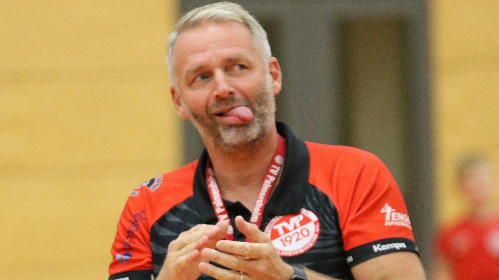 Der Trainer klatscht in die Hände, seine Zunge hat er ausgestreckt.