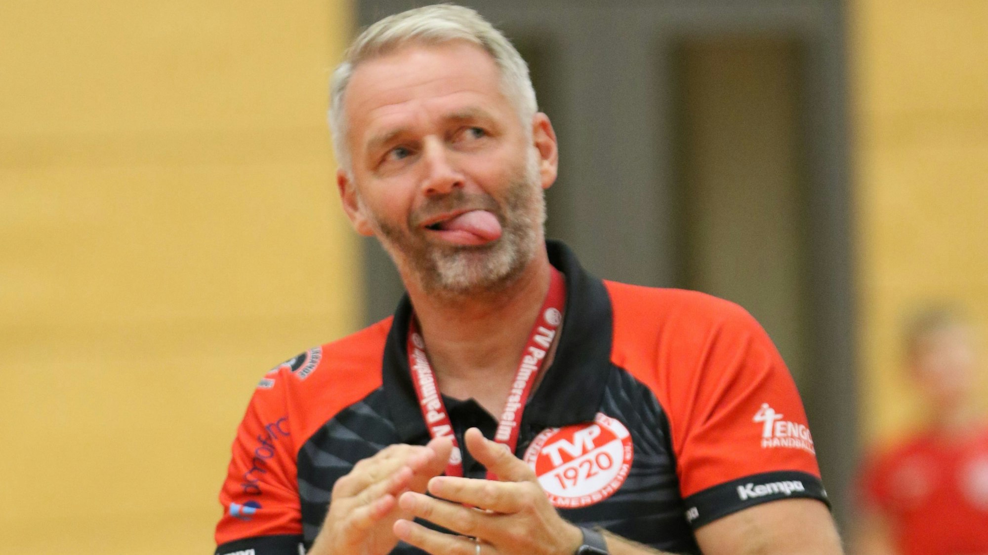 Der Trainer klatscht in die Hände, seine Zunge hat er ausgestreckt.