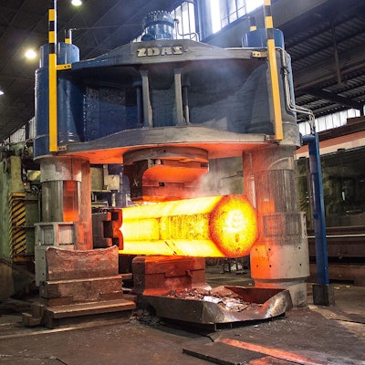 Ein glühender Block Stahl kommt aus einer Presse.