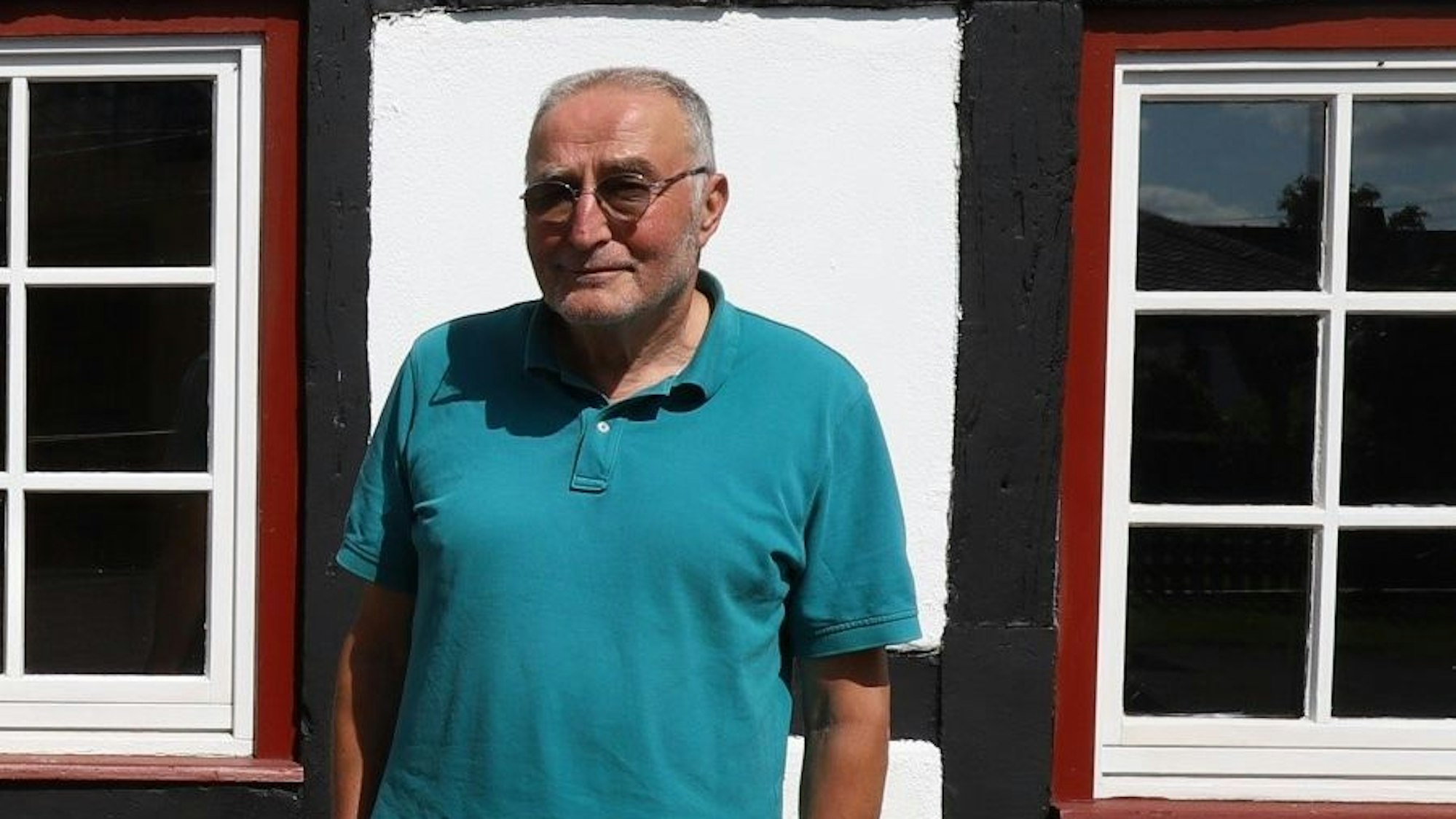 Ein Mann mit Brille steht vor einem Fachwerkhaus.