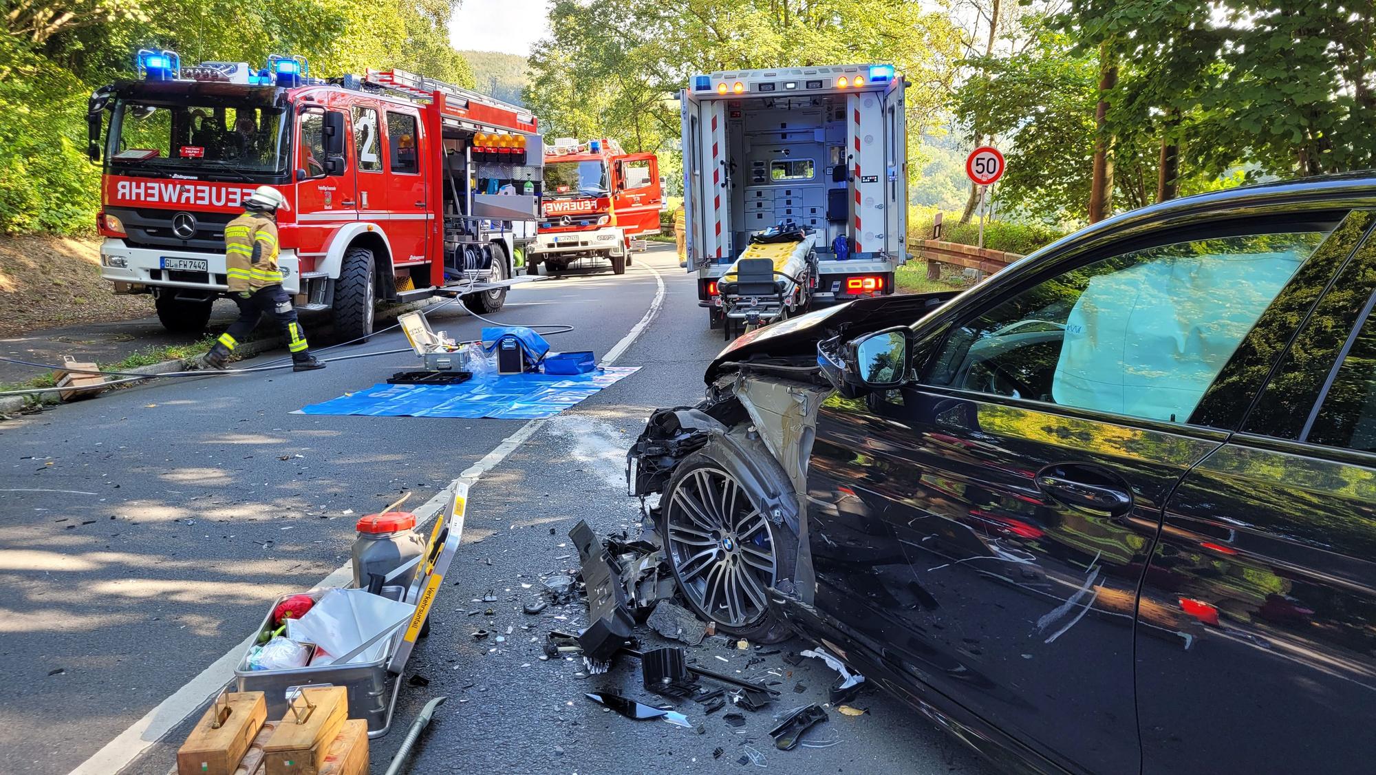 Ein Auto mit Totalschaden steht vor Feuerwehrfahrzeugen.