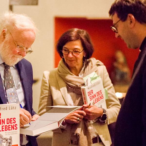 Manfred Lütz ist links im Bild, er signiert ein Buch. Neben ihm stehen eine Frau und ein Mann.
