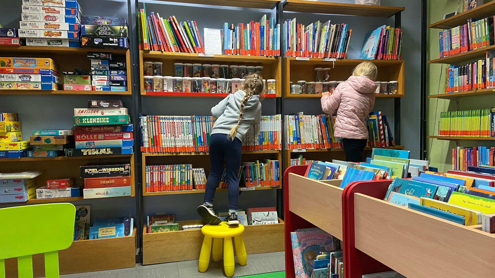Zu sehen sind zwei Kinder, die vor einem großen Bücherregal stehen.