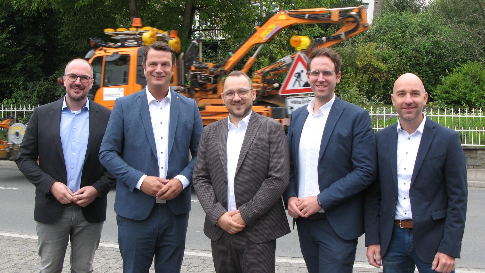 Fünf Männer stehen nebeneinander an einer Straße.