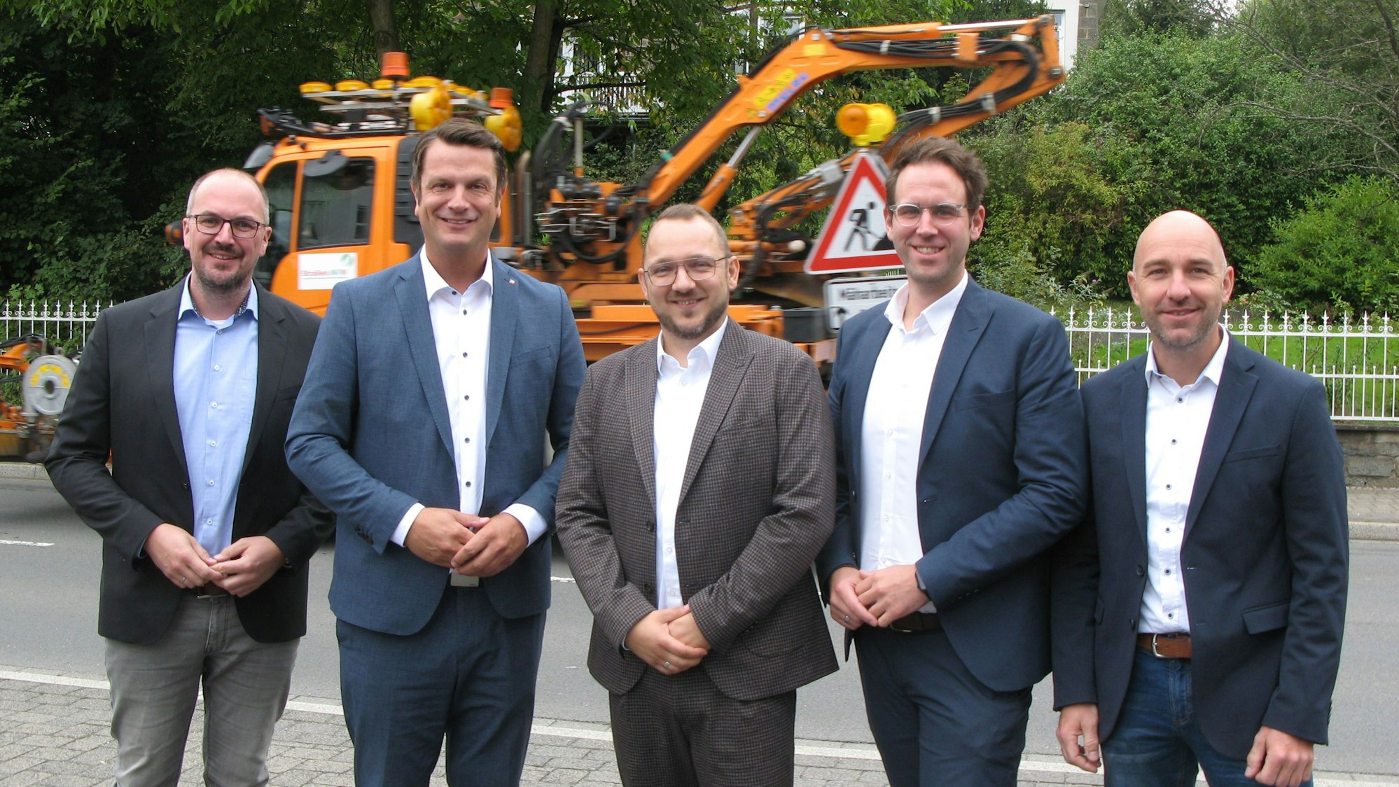 Fünf Männer stehen nebeneinander an einer Straße.