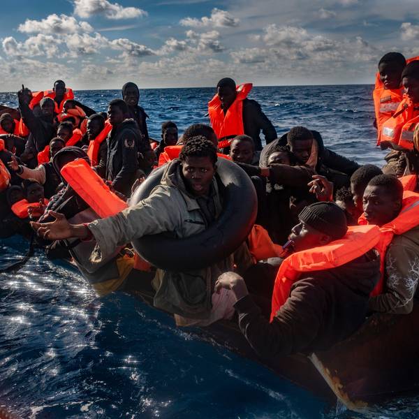 Mehrere Migranten sitzen in einem Boot im Mittelmeer, während Rettungskräfte versuchen ihnen zu helfen