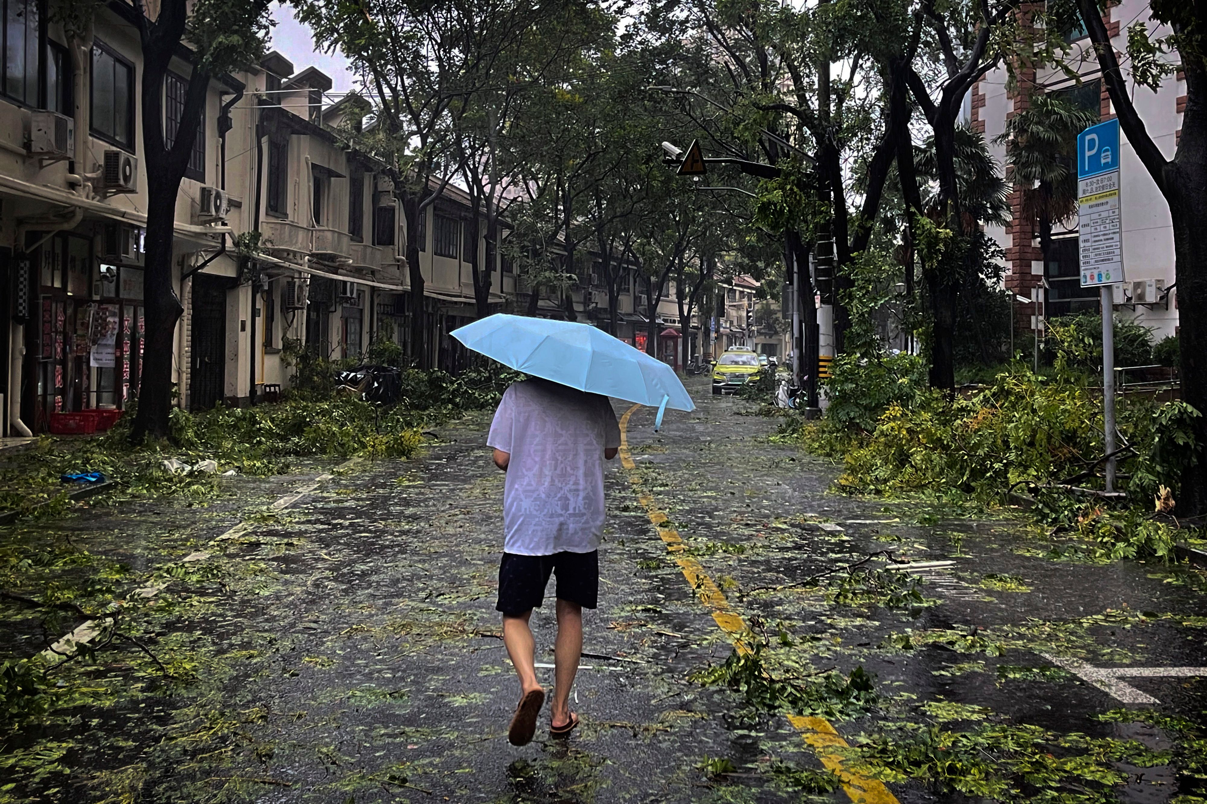Ein Mann mit Regenschirm läuft über eine Straße, die von abgebrochenen Ästen übersät ist.