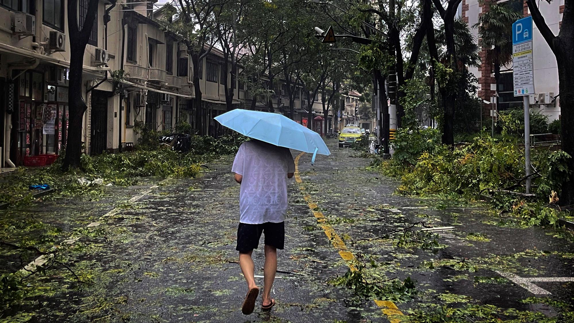 Ein Mann mit Regenschirm läuft über eine Straße, die von abgebrochenen Ästen übersät ist.