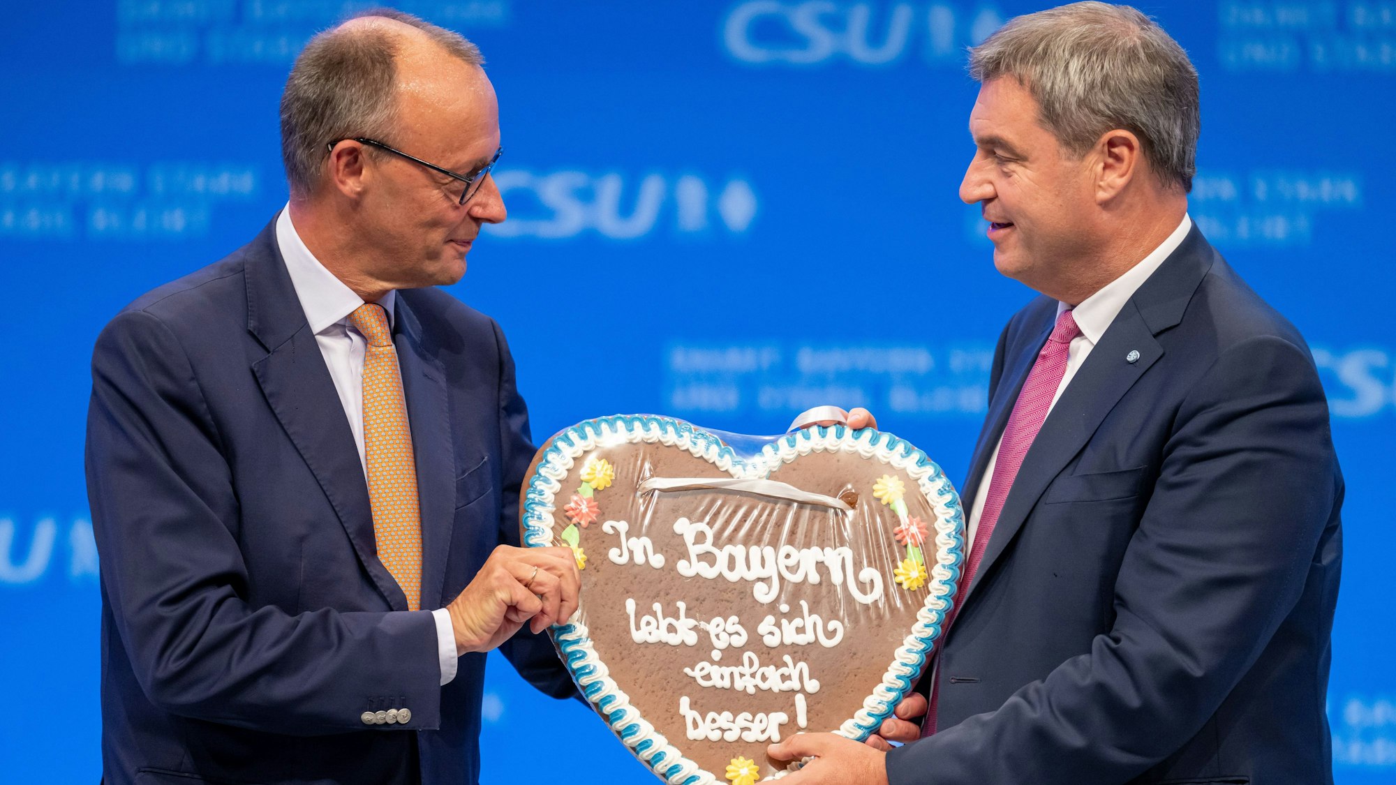 ARCHIV - 23.09.2023, Bayern, München: Friedrich Merz (l), CDU-Vorsitzender, bekommt auf dem Parteitag der CSU von Markus Söder, CSU-Parteivorsitzender, ein Lebkuchenherz mit der Aufschrift ·In Bayern lebt es sich einfach besser!· geschenkt. (zu dpa: «K-Frage der Union: Bayern wollen viel lieber Söder als Merz») Foto: Peter Kneffel/dpa +++ dpa-Bildfunk +++