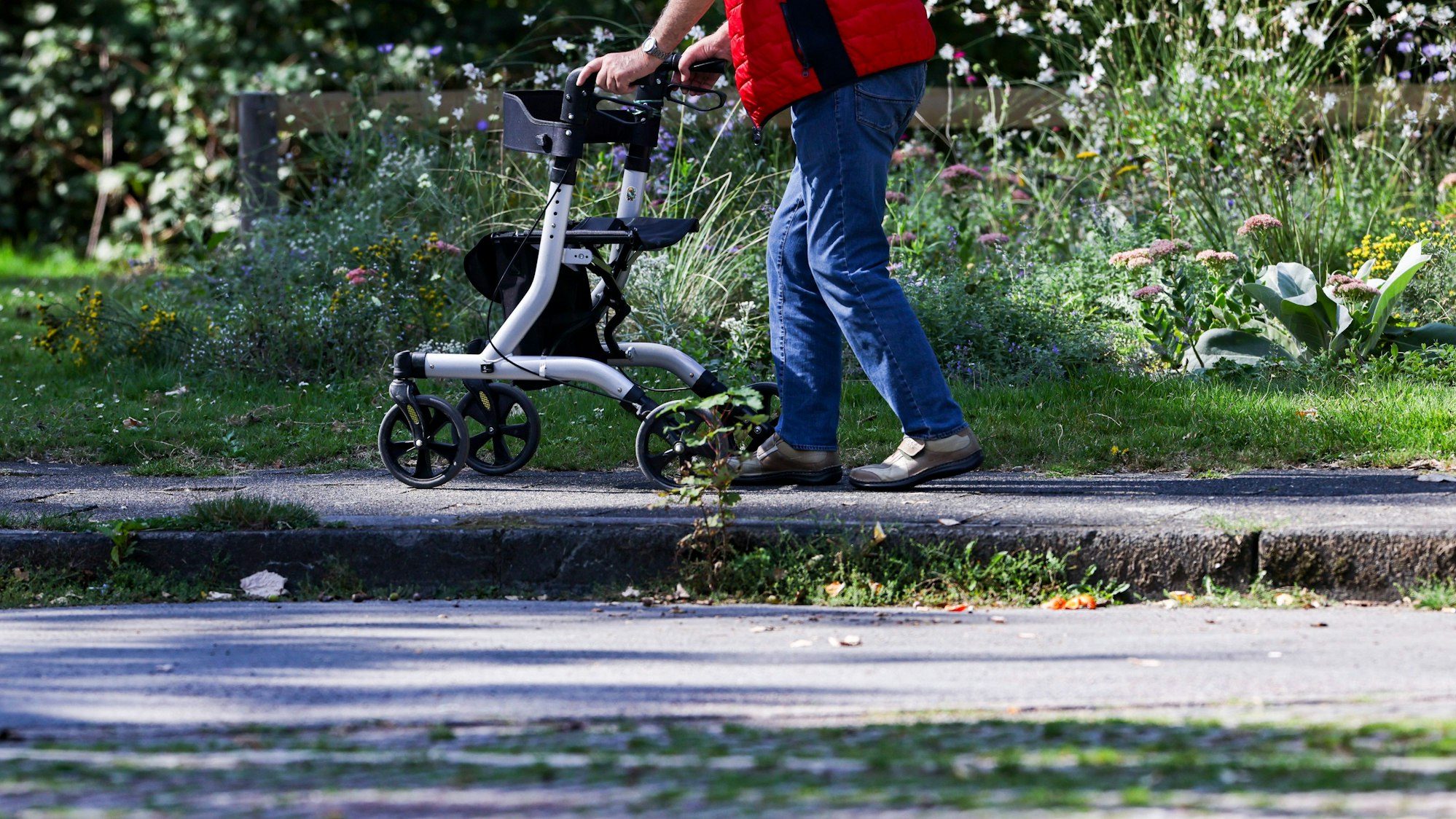 Ein Mann geht mit einem Rollator durch einen kleinen Park.