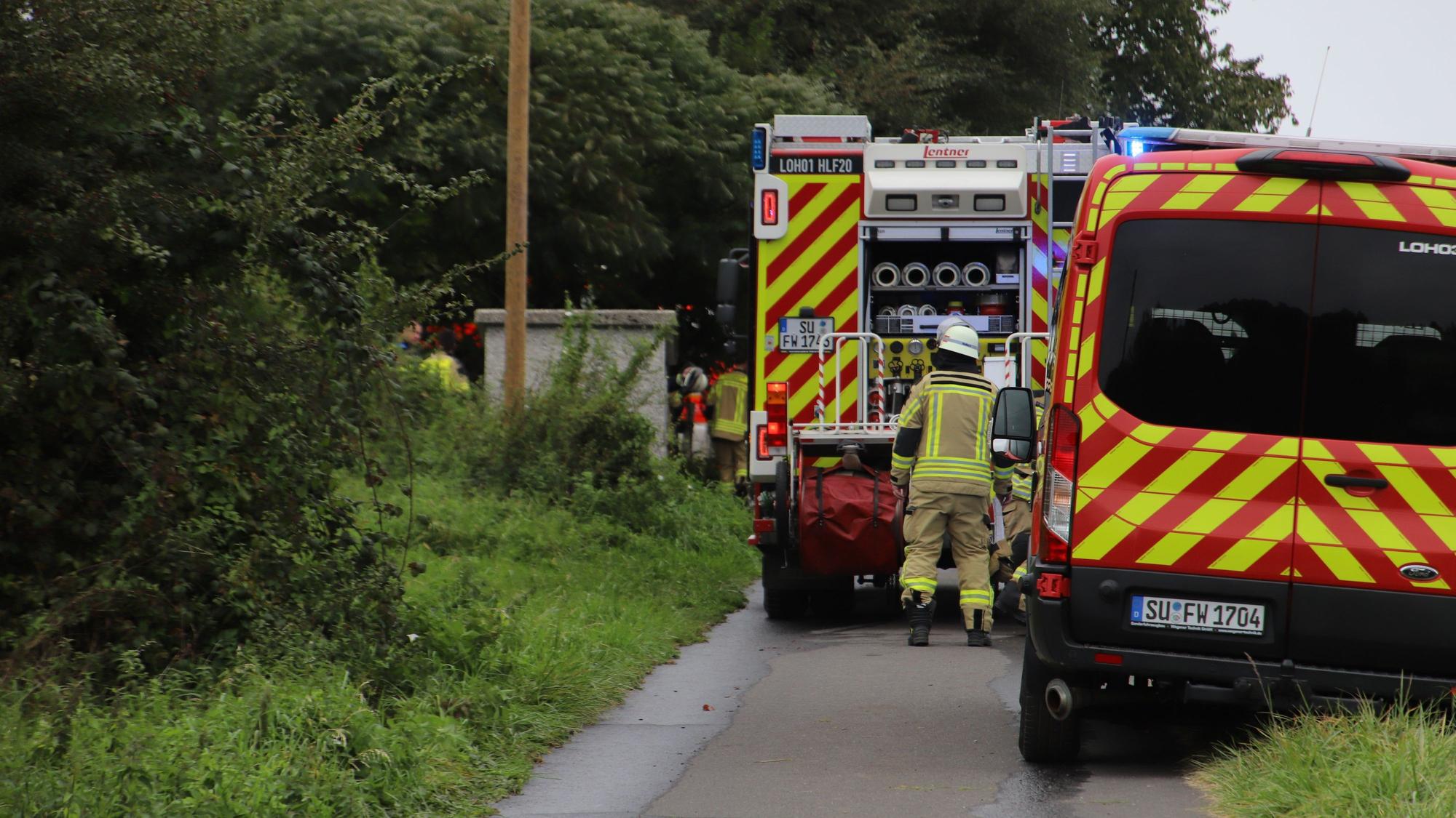 Feuerwehrleute stehen an ihren Fahrzeugen.