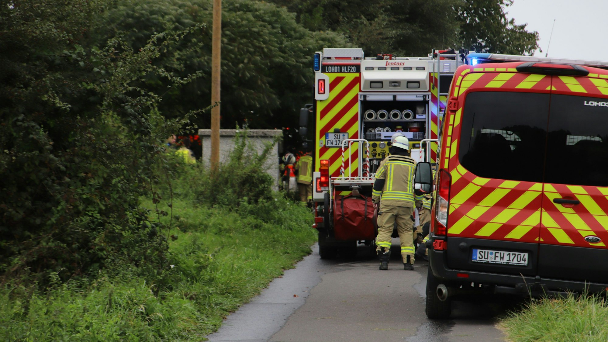 Feuerwehrleute stehen an ihren Fahrzeugen.