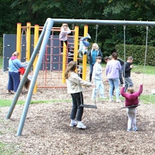 Ein Spielplatz mit Kindern, Erwachsenen, Schaukeln und Klettergerüsten.