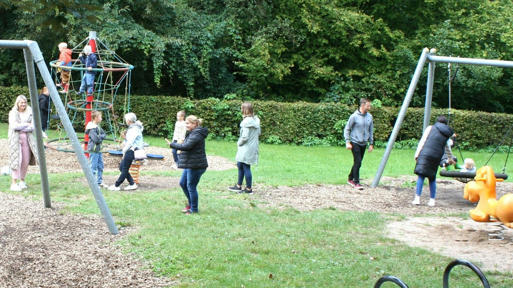 Ein Spielplatz mit Eltern, Kindern und Spielgeräten.