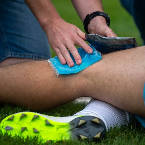 Das Bild zeigt ein Fußballerbein, das gleich mit zwei Kühlpacks gekühlt wird.