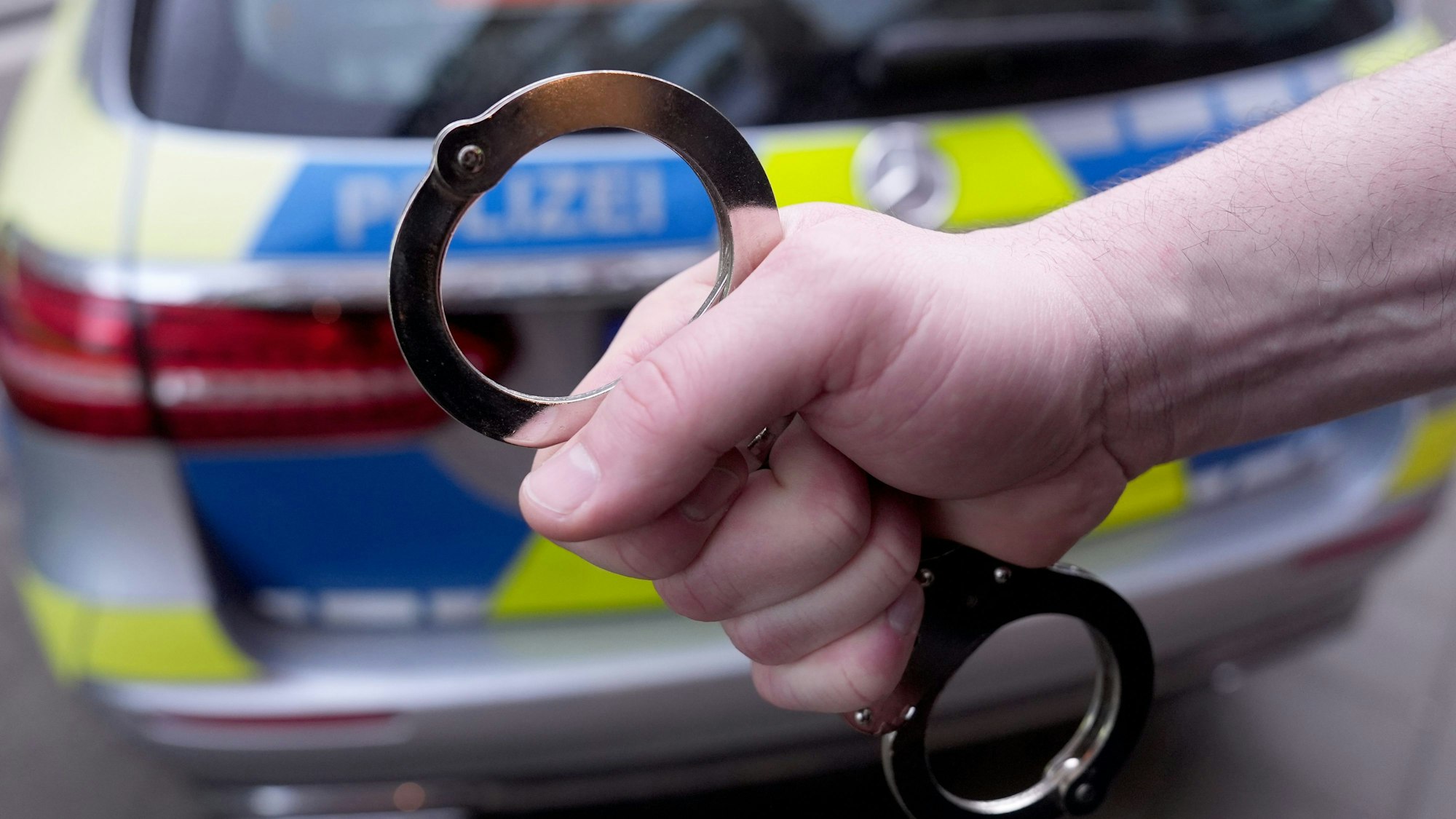 Ein Polizist hält Handschellen vor einem Einsatzfahrzeug hoch.