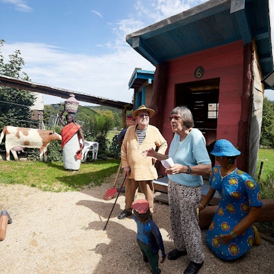 Rita und Paul Greven bei der Eröffnung des Friedensdorfes in ihrem Skulpturenpark. Man erkennt unter anderem Skulpturen von Kühen, einem arbeitenden Mann, einer Frau mit einem Gefäß auf dem Kopf.