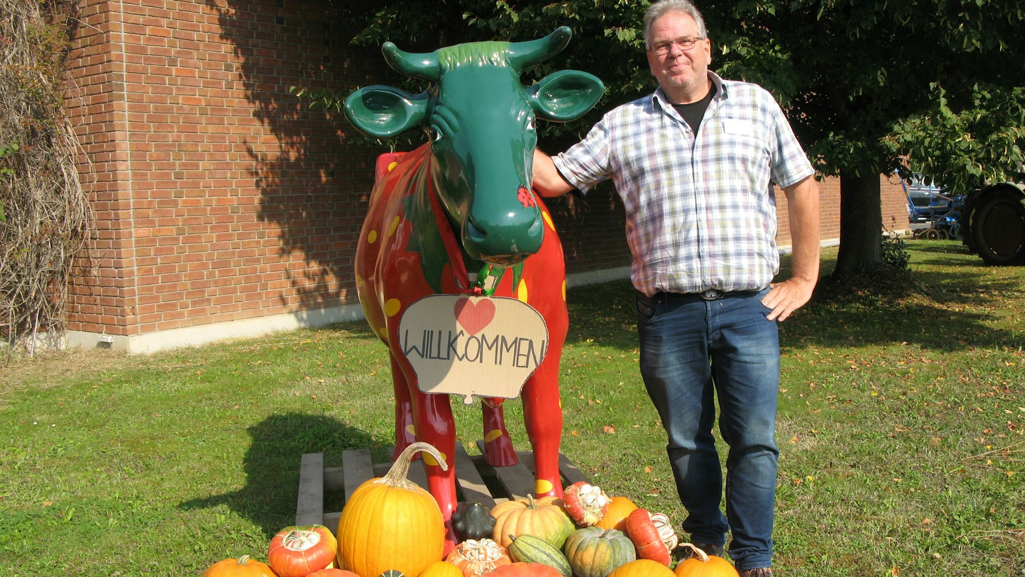 Landwirt Karl-Josef Engels neben einer roten Kuhskulptur und einem bunten Kürbisfeld.