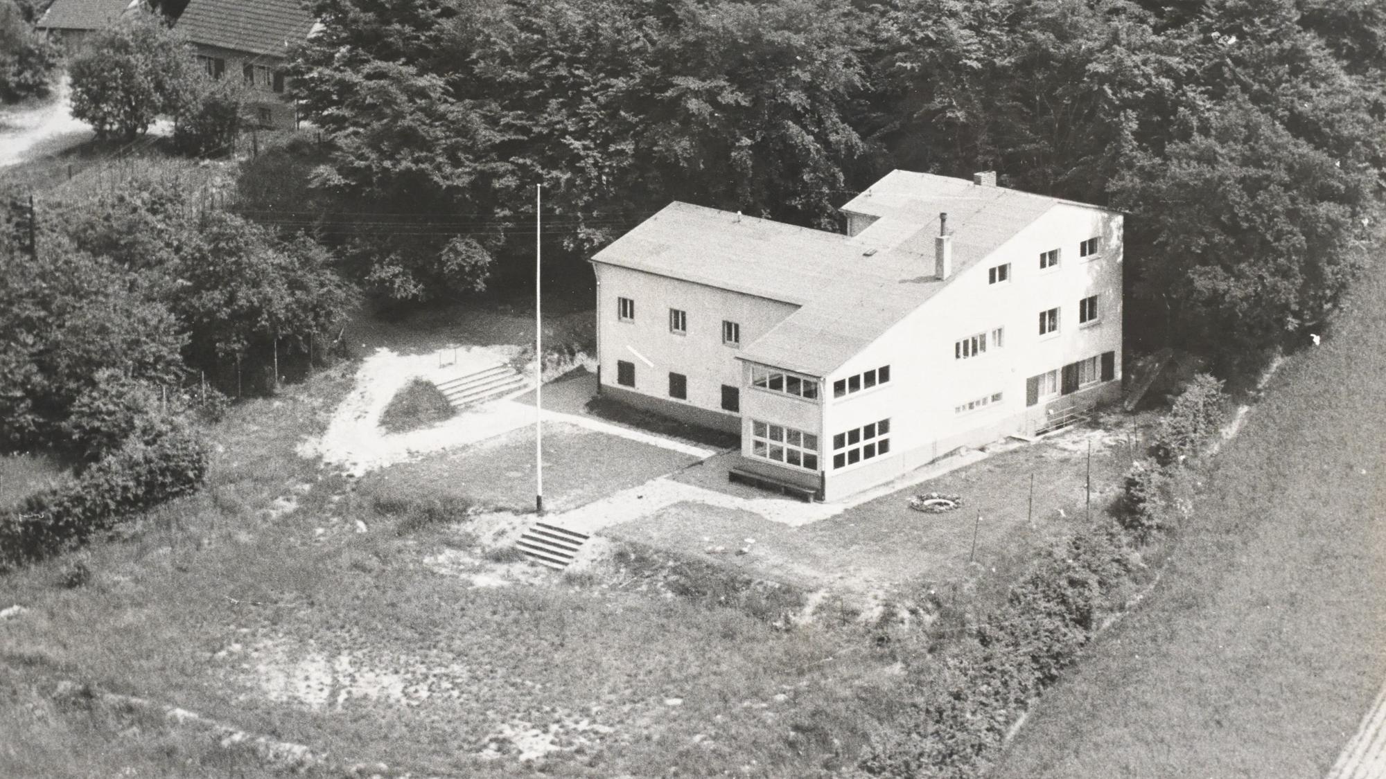 Ein weißer Neubau der 40er oder 50er Jahre mit einem noch kahlen Baugrundstück.