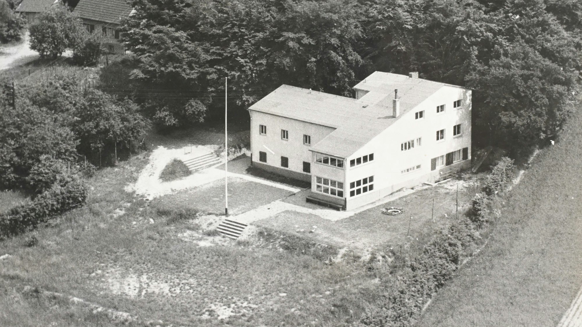 Ein weißer Neubau der 40er oder 50er Jahre mit einem noch kahlen Baugrundstück.