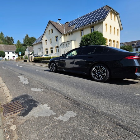 Zu sehen ist die Straße mit vielen geflickten Stellen. Zwei Autos kommen sich entgegen.