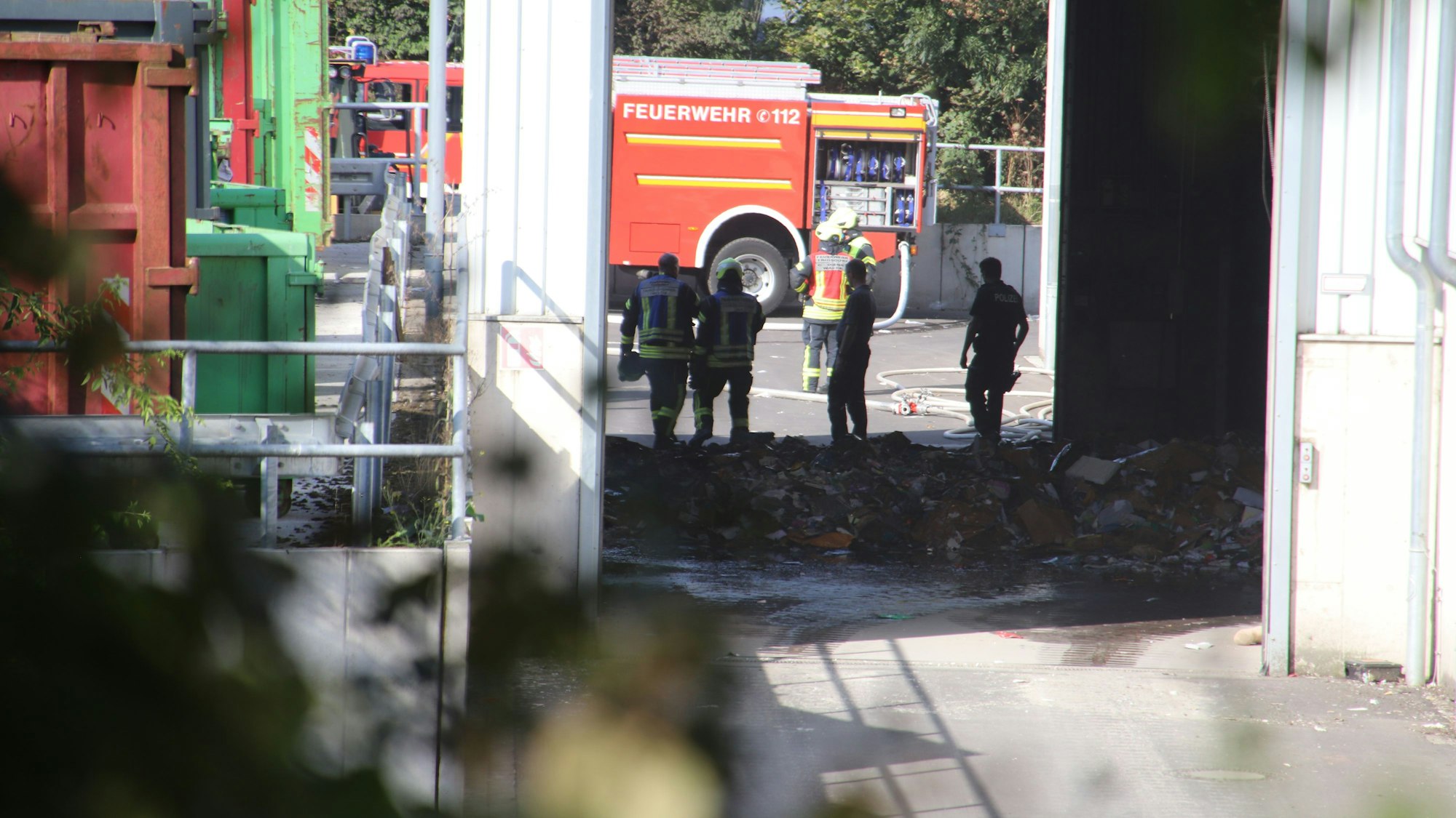 Feuerwehrleute und Polizisten stehen vor einem Papierhaufen, der gebrannt hat.