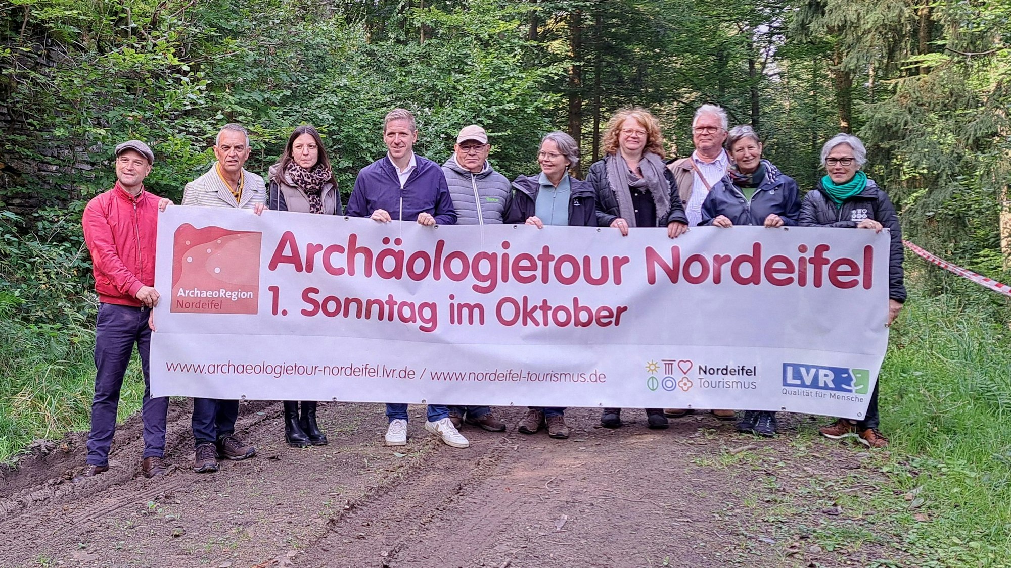 Eine Gruppe Menschen steht im Wald und hält ein Transparent, das für die Archäologietage wirbt.