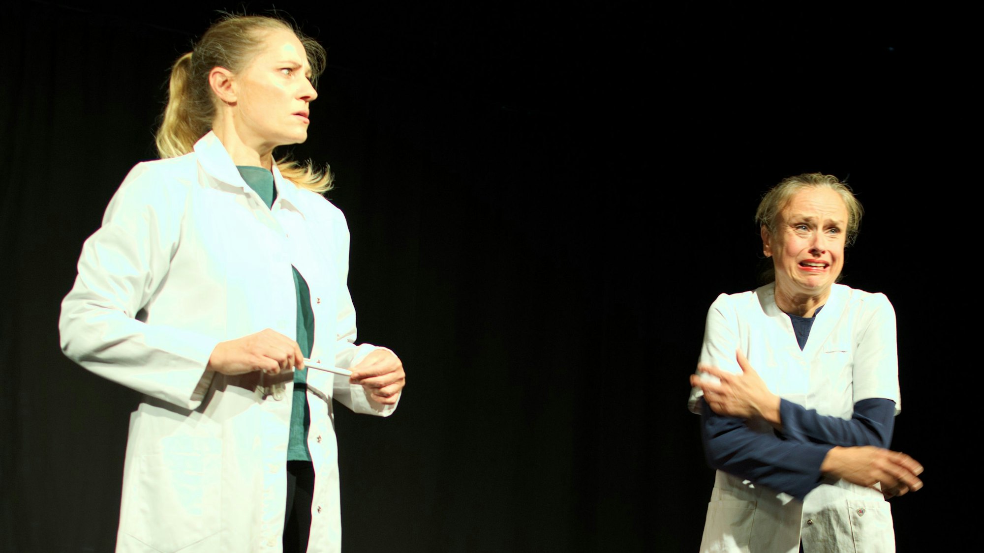 Die Künstlerinnen Melanie Haupt (l.) und Judith Jakob stehen nebeneinander in weißen Kitteln auf der Bühne.