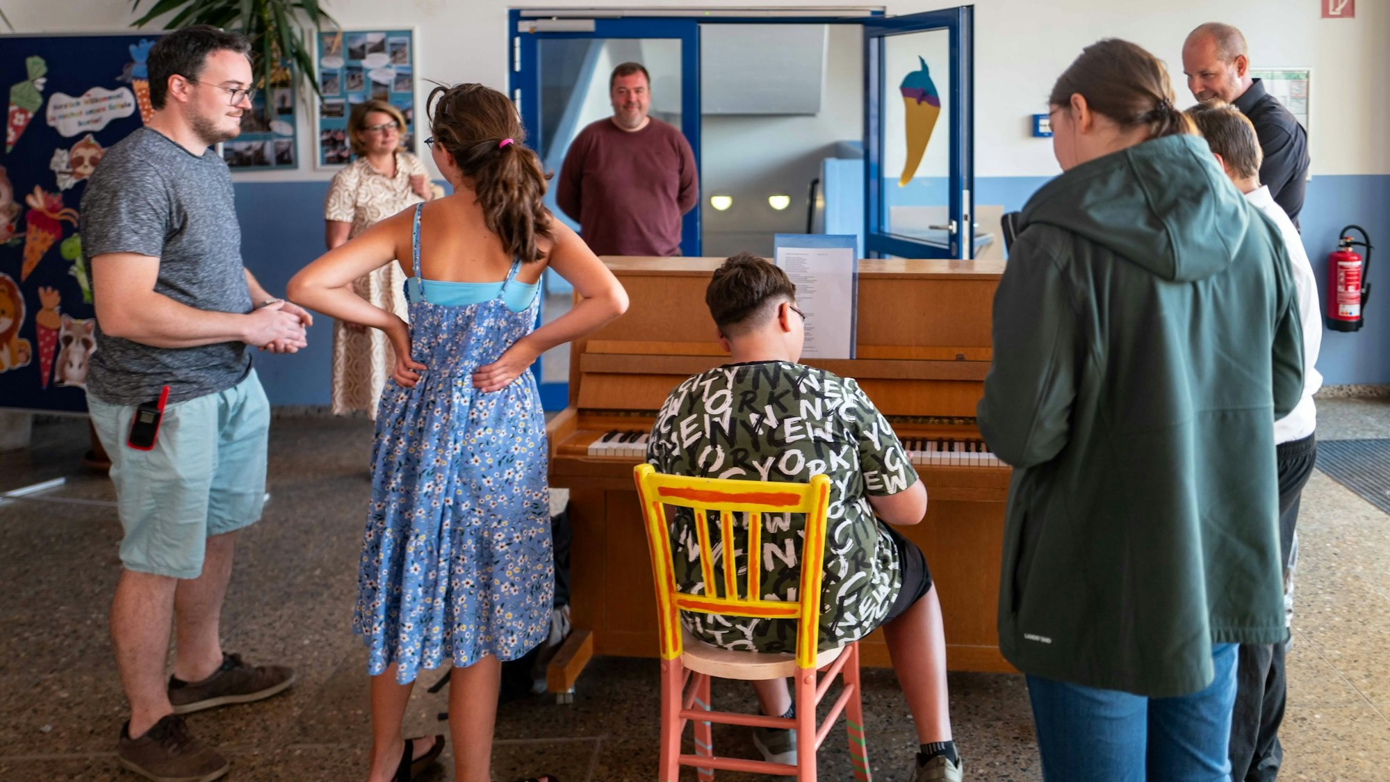 Das Bild zeigt einen Schüler am Klavier in der Matthias-Hagen-Schule. Lehrer und weitere Schüler stehen um das Instrument herum und lauschen der Musik.