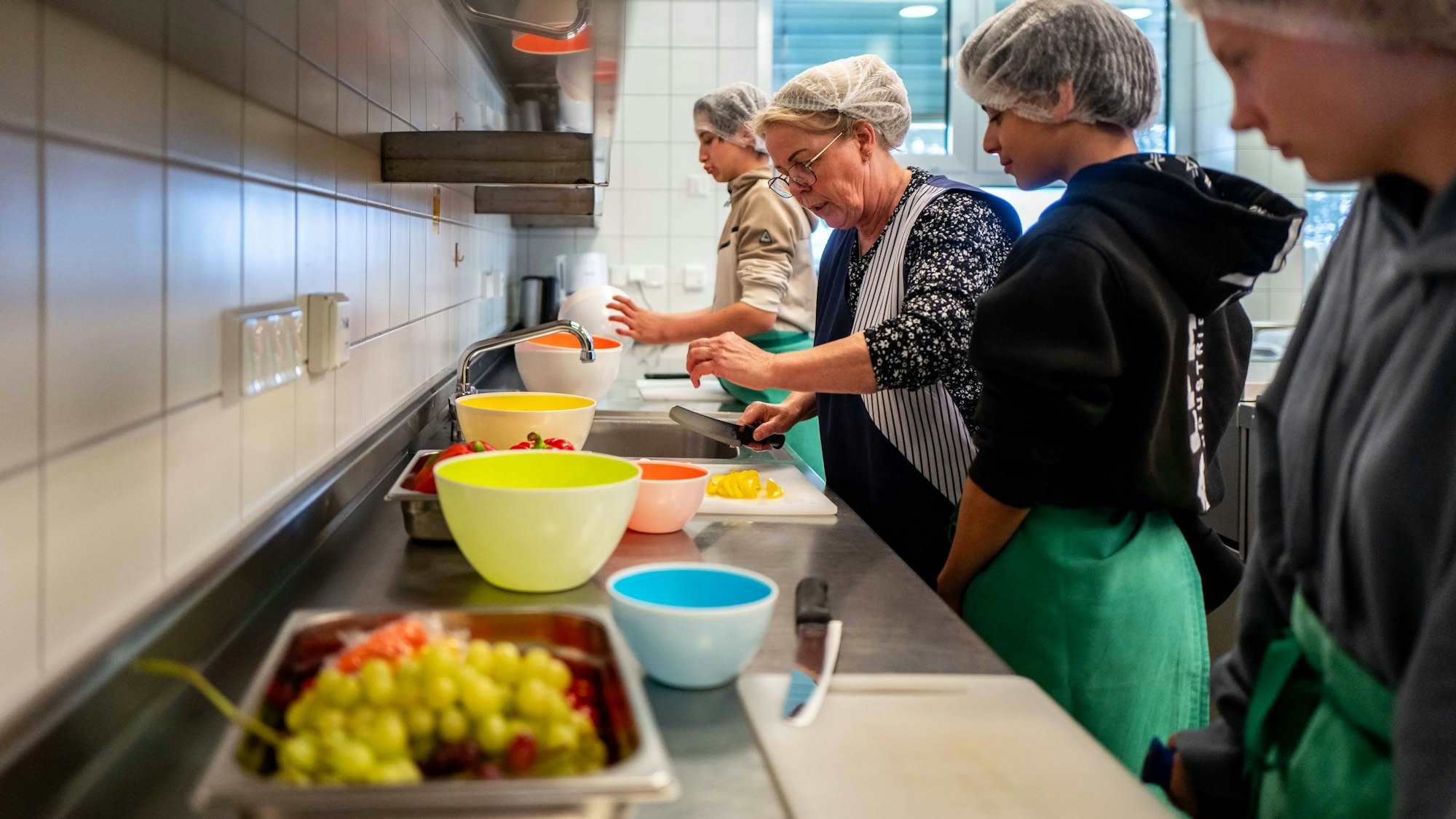 Das Bild zeigt drei Schüler der Stephanus-Schule in Bürvenich beim Schnippeln in der Schulküche. Unterstützt werden sie von einer Lehrerin.