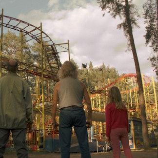 Zwei Männer und zwei Kinder stehen vor einer maroden Achterbahn.