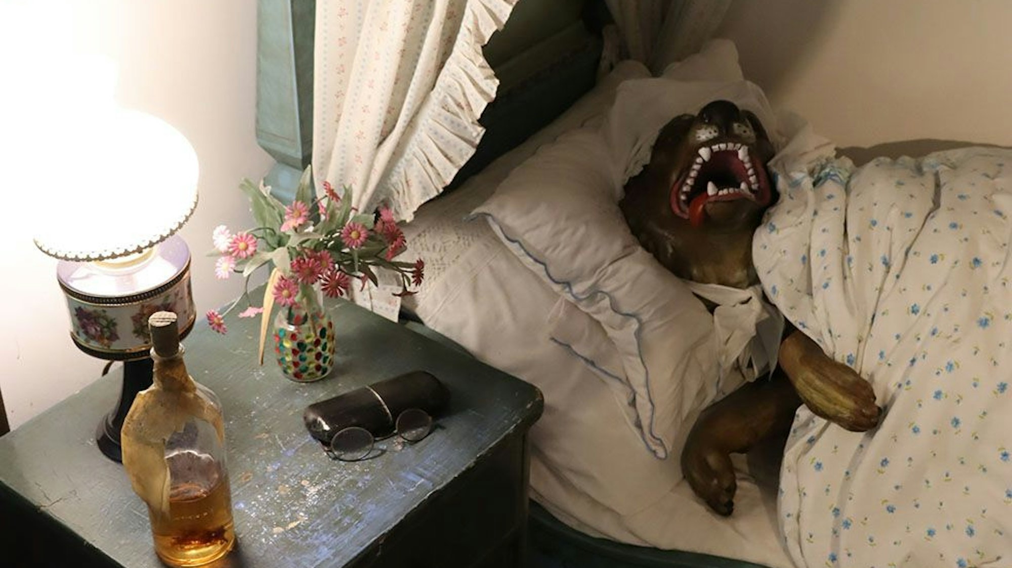 Eine Szene im Märchenwald: Der Wolf liegt als Großmutter verkleidet im Bett. Er sperrt das Maul auf und zeigt seine Zähne.