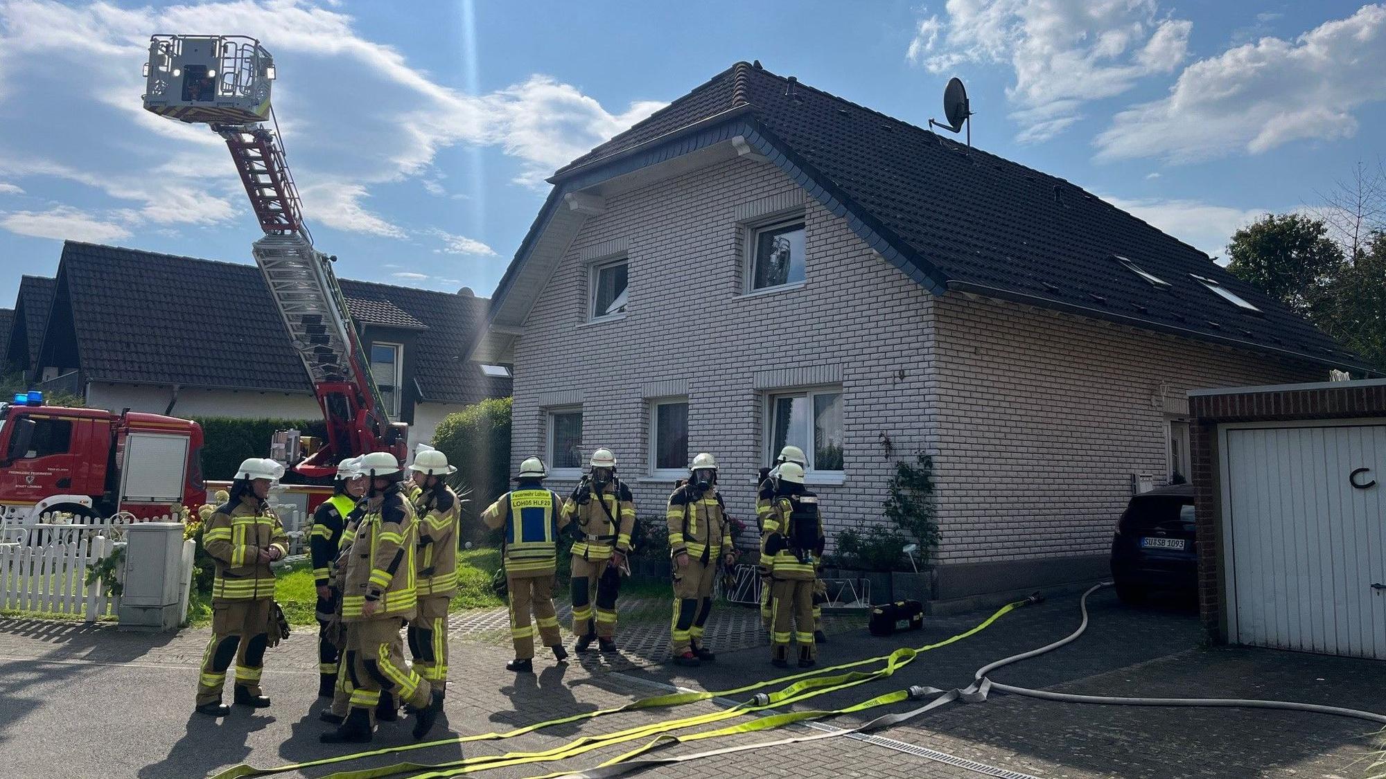 Feuerwehrleute und eine Drehleiter stehen vor einem Haus.