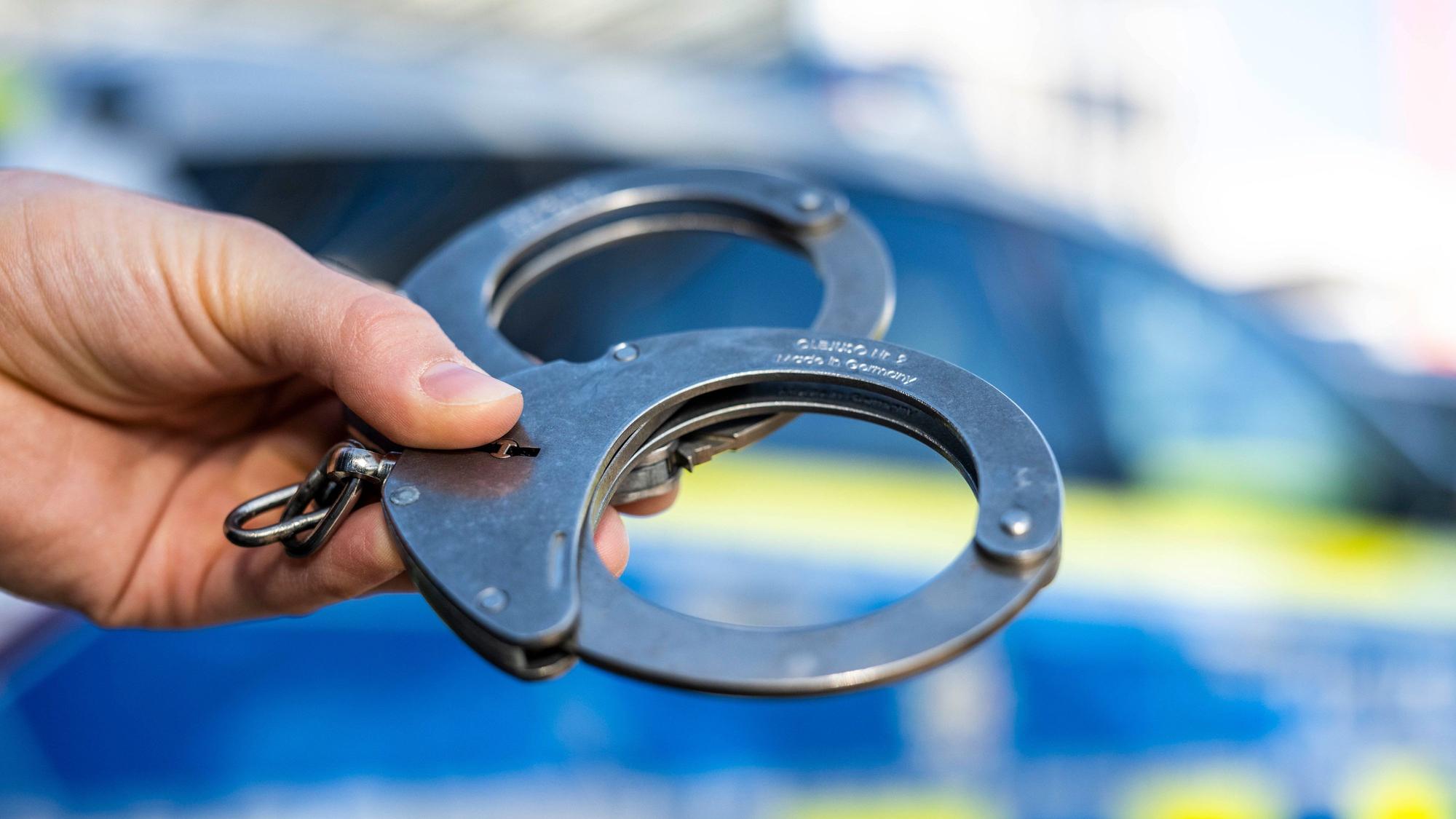 Handschellen vor einem Polizeifahrzeug.