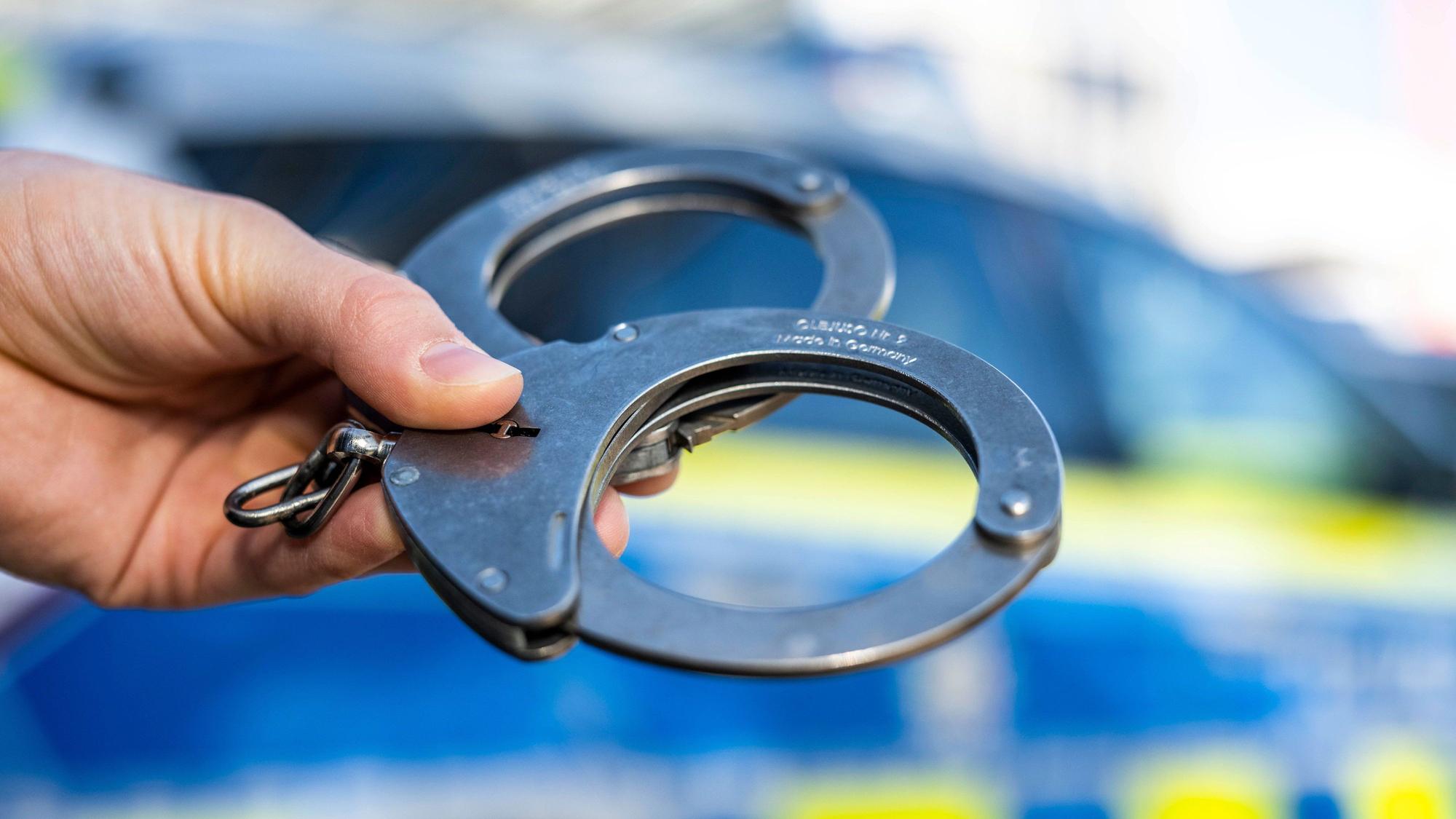 ILLUSTRATION - 28.09.2021, Nordrhein-Westfalen, Gütersloh: Eine Hand hält Handschellen vor einen Streifenwagen der Polizei. (zu dpa: «Zahl der Intensivstraftäter in NRW gestiegen») Foto: David Inderlied/dpa +++ dpa-Bildfunk +++