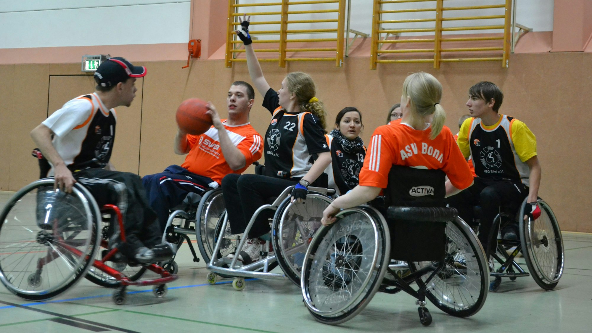 Mehrere Jugendliche spielen Rollstuhlbasketball in einer Turnhalle.